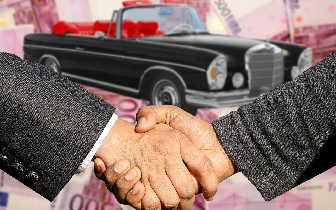Image avec deux hommes se serrant la main avec une voiture ancienne en arrière plan.