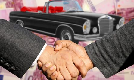 Image avec deux hommes se serrant la main avec une voiture ancienne en arrière plan.