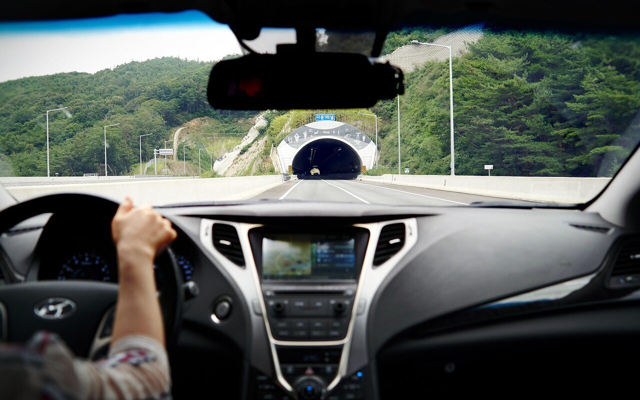 Intérieur d'une voiture avec un conducteur sur une route au loin il y a un tunnel