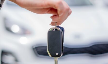 Une main tient une clé de voiture avec une voiture en fond d'écran
