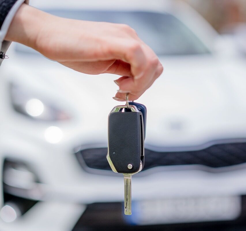 Une main tient une clé de voiture avec une voiture en fond d'écran